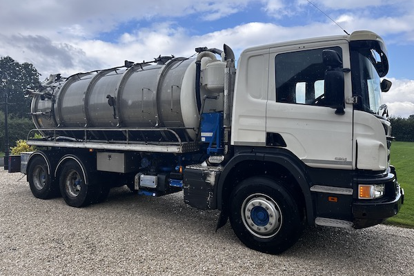 A large truck with a cylindrical tank attached, parked on gravel.